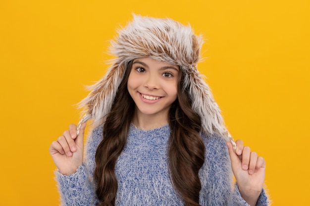 Teen girl in knitwear on yellow background. portrait of child wearing warm clothes. express positive emotion. winter fashion. happy cute kid with curly hair in earflap hat. female fashion model.