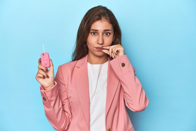 Teen girl in pink proudly holding her car key with fingers on lips keeping a secret