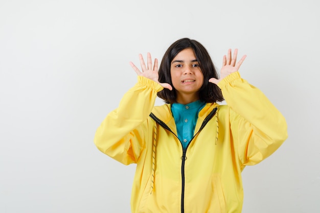 Teen girl showing surrender gesture in yellow jacket and looking cheerful , front view.