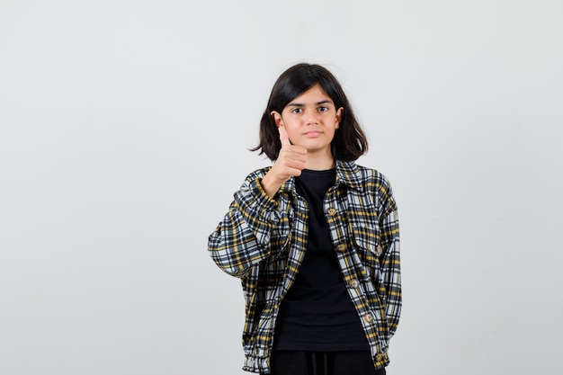 Teen girl showing thumb up in casual shirt and looking merry. front view.