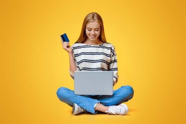 Photo teen girl sitting on floor with laptop and credit card