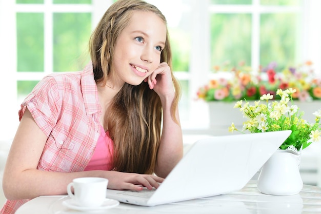 Teen girl sitting at table and using laptop