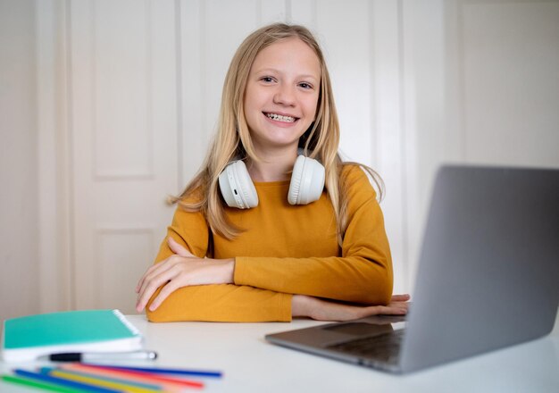 Teen girl sitting at table with laptop and headphones