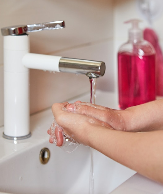 Teen girl washes hands with soap in the sink. Protect against viruses and bacteria