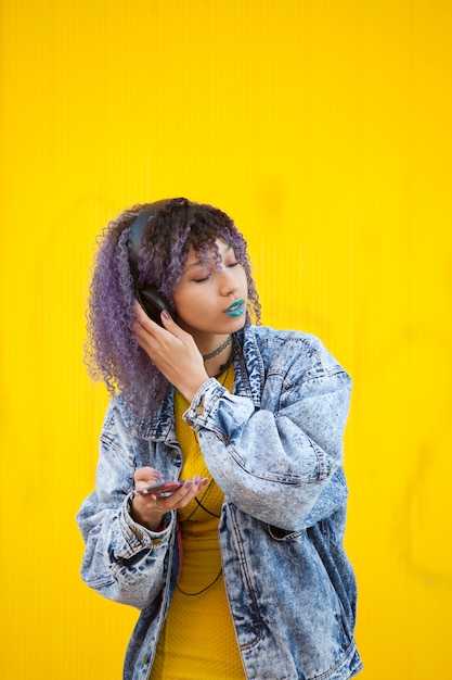 Teen girl with afro hair listening to music on a yellow wall