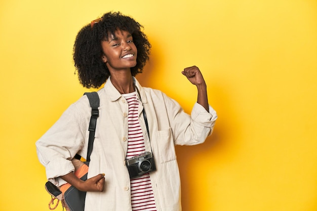 Teen girl with backpack camera ready for vacation raising fist after a victory winner concept