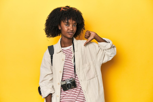 Teen girl with backpack camera ready for vacation showing a dislike gesture thumbs down