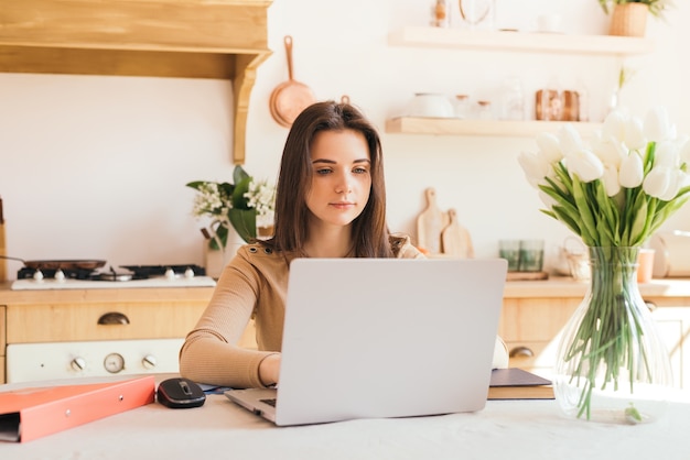 Teen girl with laptop doing homework in bright kitchen remote work and freelance work