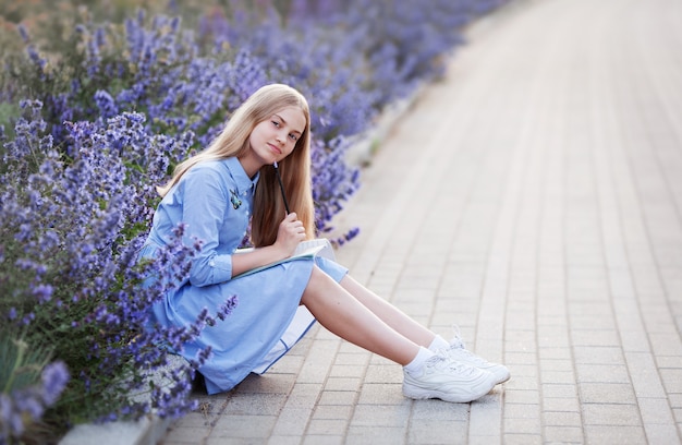 Teen girl with pen writes in a notebook, sitting in the Park in blue lavender flowers outside