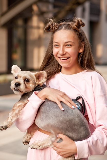 Teen girl with pet animal small dog holding in a hands outdoor in a park.