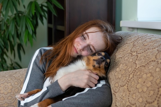 Teen girl with red hair, generation Z, crying at home in an embrace with a dog