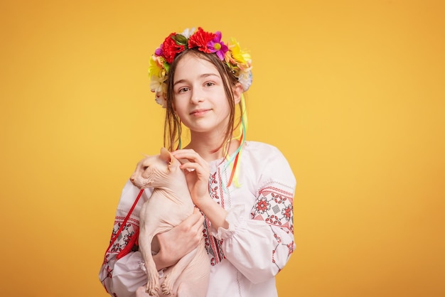 Teen girl with a wreath on her head and dressed in an embroidered shirt with a cat in her arms Pet