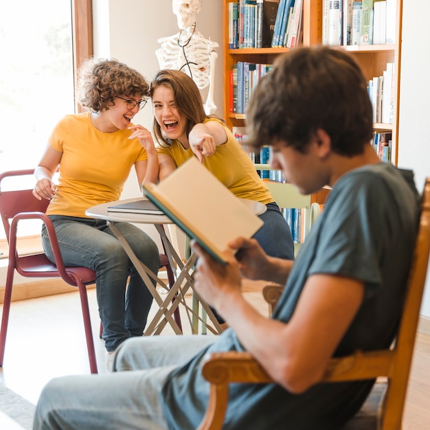 Teen girls laughing and pointing at reading boy