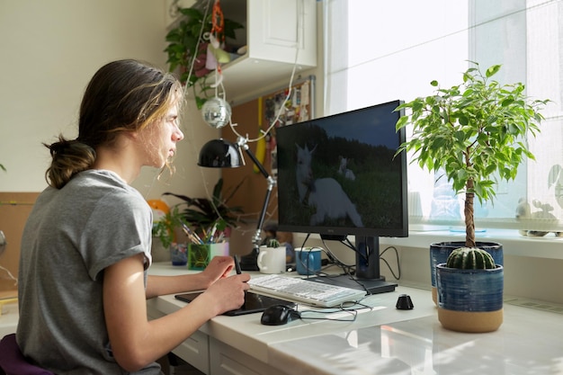 Teen guy at home working on computer using graphics tablet to work with images