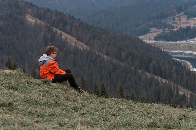 Teenage alone boy sits on hillside and looking at the distance thinks about something Travelling with children