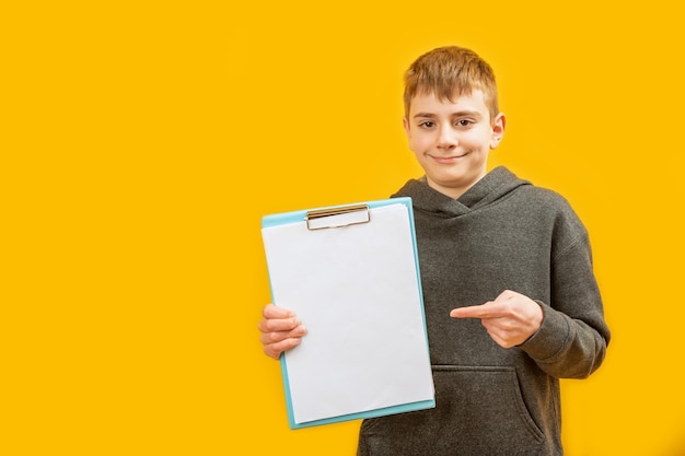 Teenage boy in casual clothes holds blank sheet of paper and points his index finger at it Copy space Mock up