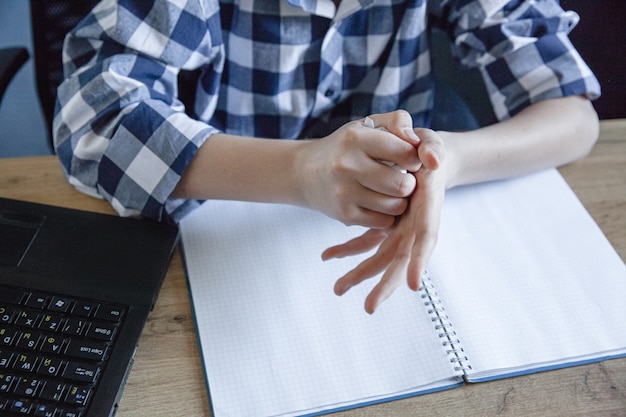 A teenage boy in a checked shirt in the process of home training tore a sheet from a notebook and crumples it in his hands.