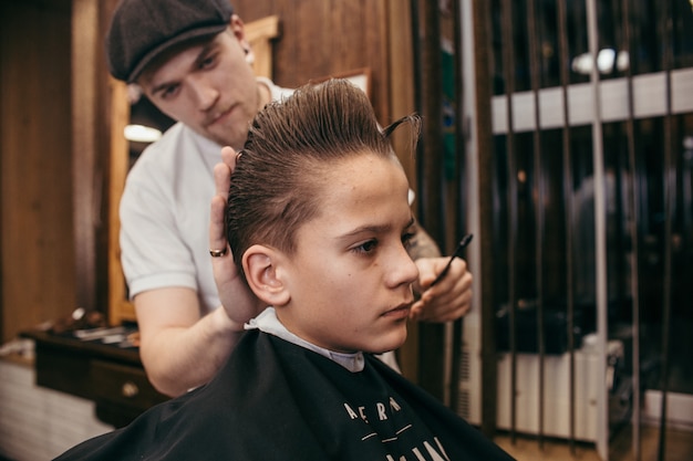 Teenage boy haircuts hairdresser in the Barber shop. Fashionable stylish retro hairstyle. Portrait of a child with a beautiful haircut. Russia,