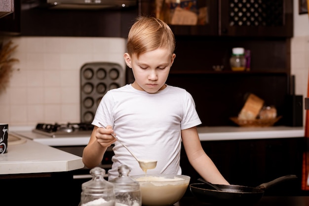 Teenage Boy in the kitchen at home making dough for pancakes pastry Children cooking concept