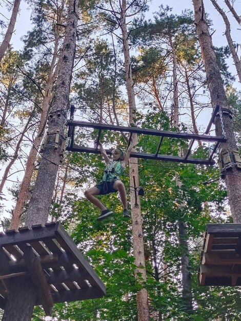 A teenage boy in a rope park in an amusement park moves on a suspended handrail View from below