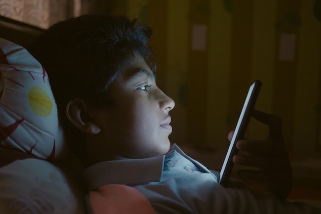 Teenage boy sitting on sofa using smart phone at night