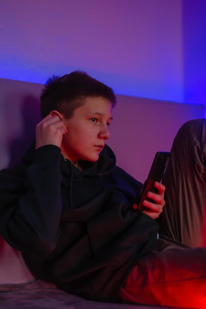 Teenage boy using phone and headphone in his room with neon light