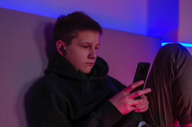 Teenage boy using phone in his room with neon light