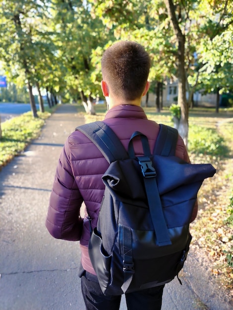 A teenage boy with a backpack goes to school on the street Rear view in perspective