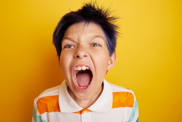 Teenage boy with glasses screaming over isolated light yellow background