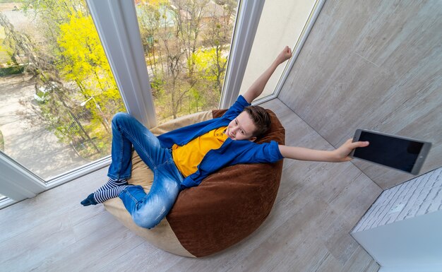 Teenage boy won the video game. Kid relaxing at balcony with green trees outside.