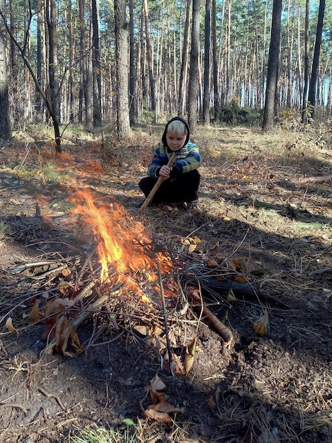 A teenage Caucasian boy is warming himself by a burning fire He is in the forest and has dyed hair