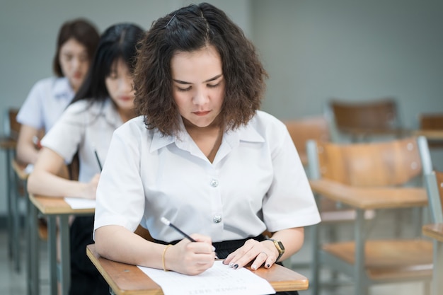 Teenage college students write on examination paper answer sheet in the classroom