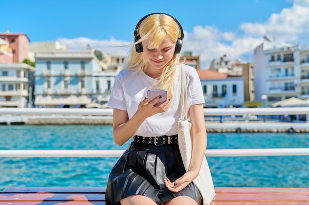 Teenage female in headphones with smartphone on the embankment