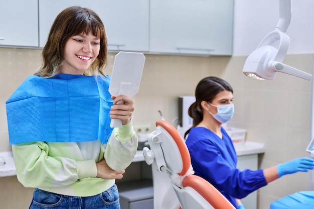 Teenage female looking at healthy teeth in mirror in dental office