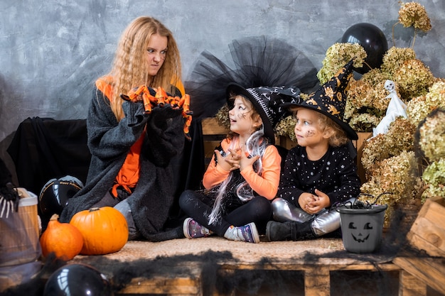 Photo teenage girl among decor for halloween holiday with two sisters 4-5 years old have fun on background of black and orange decorations, humor photo