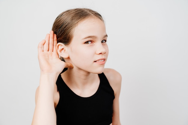 A teenage girl in a black T-shirt holds her hand by her ear and listens.