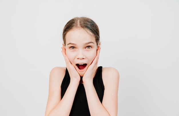 A teenage girl in a black T-shirt is surprised and her hands are at the face.