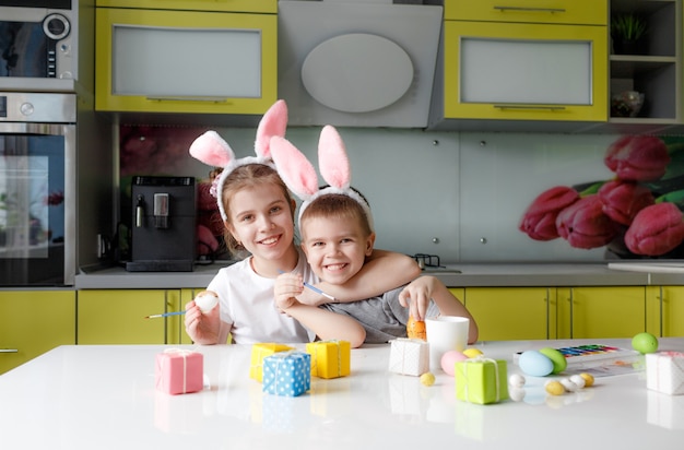 A teenage girl and boy with rabbit ears on their head paint eggs