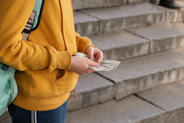 Teenage girl counts dollar bills on the background of the stairs