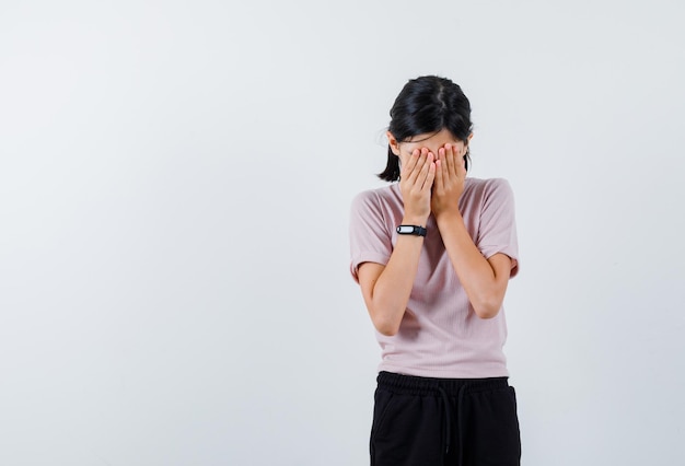 Teenage girl covering her face with hands on white background