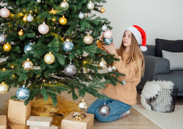 Teenage girl decorates the Christmas tree. Christmas tree in the living room.