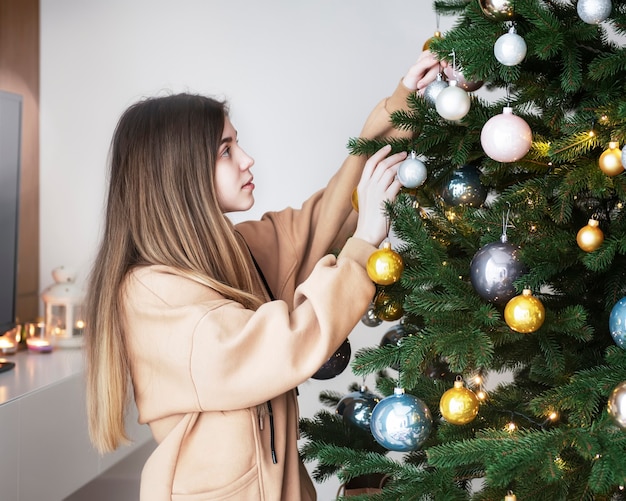 Teenage girl decorates the Christmas tree. Christmas tree in the living room.