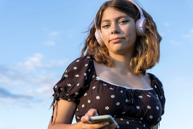 Teenage girl in a dress listens to music on her smartphone