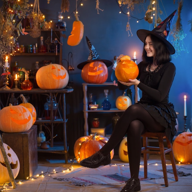 Teenage girl dressed as a witch with pumpkins on the background of decor for Halloween