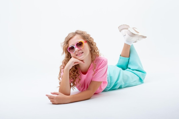 A teenage girl in heartshaped sunglasses lies on a white background