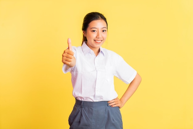 Teenage girl in high school uniform standing with thumbs up on isolated background