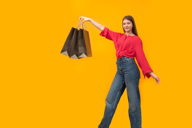 Teenage girl holds black paper bags on bright yellow background Concept of shopping Copy space