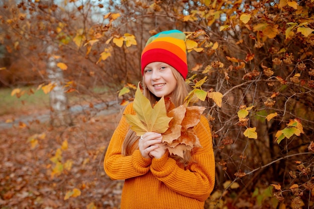 A teenage girl holds a bouquet of autumn leaves in the park in autumn