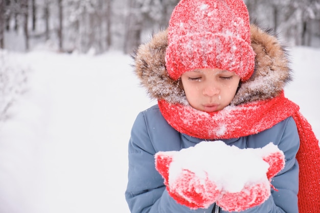 A teenage girl is blowing on the snow in her palms and fanning mittens and a knitted hat changing weather