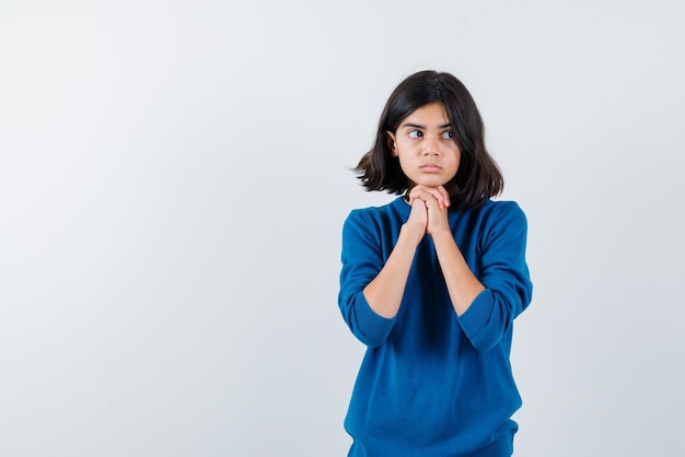 The teenage girl is looking to right by holding hands under chin on white background